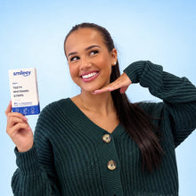Smiling model holding a Smileey PAP+ teeth whitening strip on a light blue background